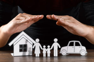 hands protecting a paper family, house, and car