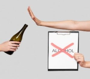 Hand stopping a bottle while holding up a sign with "alcohol" crossed out