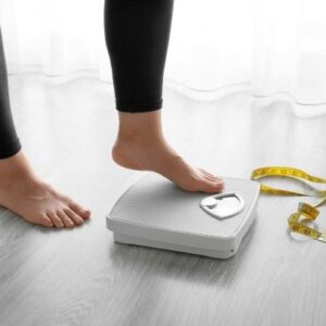 A picture of a tape measure with two human feet with one stepping onto a scale, symbolizing weight loss