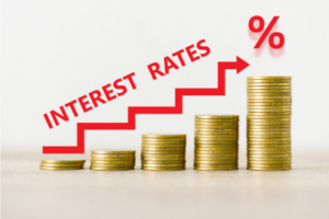 Photo of increasing stacks of gold coins with a growing arrow that says "INTEREST RATES" above it, as well as a percent symbol, symbolizing higher interest rates