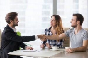 a photo of a man in professional attire shaking hands with two clients, symbolizing maintaining and fostering good relationships with clients