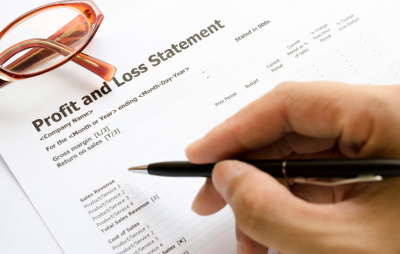 Photo of a hand with a pen reviewing a sheet titled "Profit and Loss Statement"