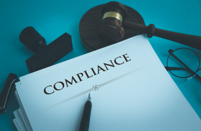 A photo of a stack of papers titled "compliance", symbolizing regulatory compliance
